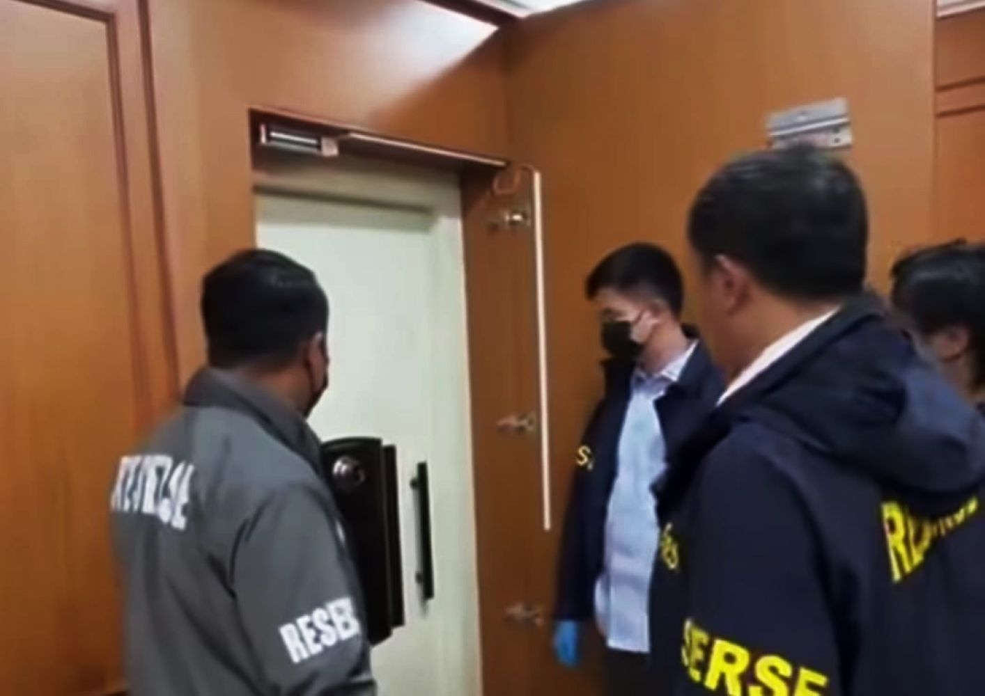 11gjaksa catrawarta Group of investigators in jackets around a bank vault door in a wood paneled room one man wears a mask and blue gloves