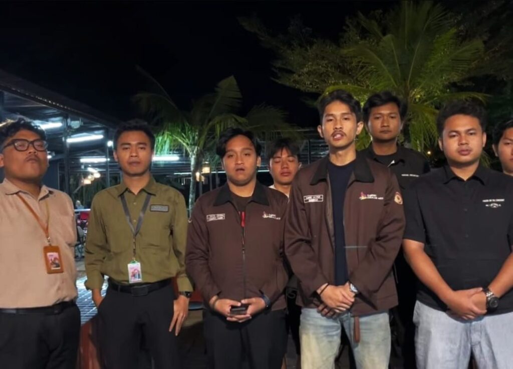 Group of seven men standing side by side at night wearing uniforms with badges palm trees in the background