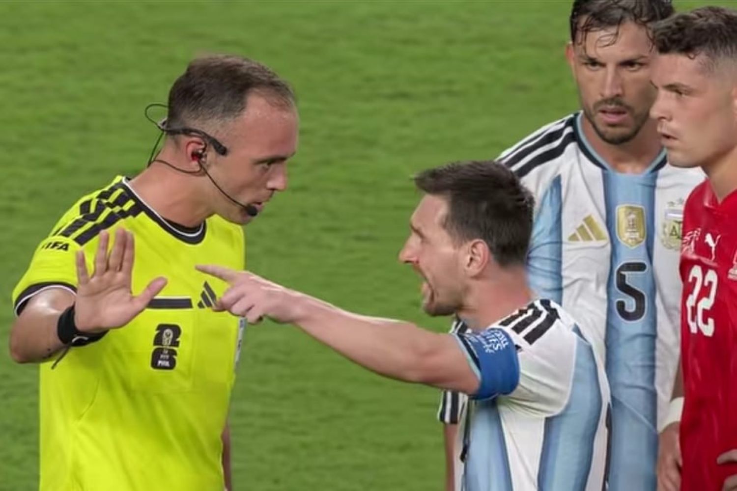 12glionel catrawarta Soccer referee in a bright yellow kit raises a hand to stop as an argentine player argues with teammates nearby