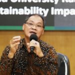 Man in a batik shirt speaks into a microphone during a sustainability panel gesturing with his hand