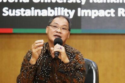 Man in a batik shirt speaks into a microphone during a sustainability panel, gesturing with his hand.