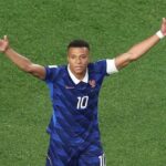French soccer player with jersey number 10 raises arms in triumph on green field
