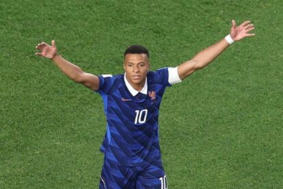 French soccer player with jersey number 10 raises arms in triumph on green field.