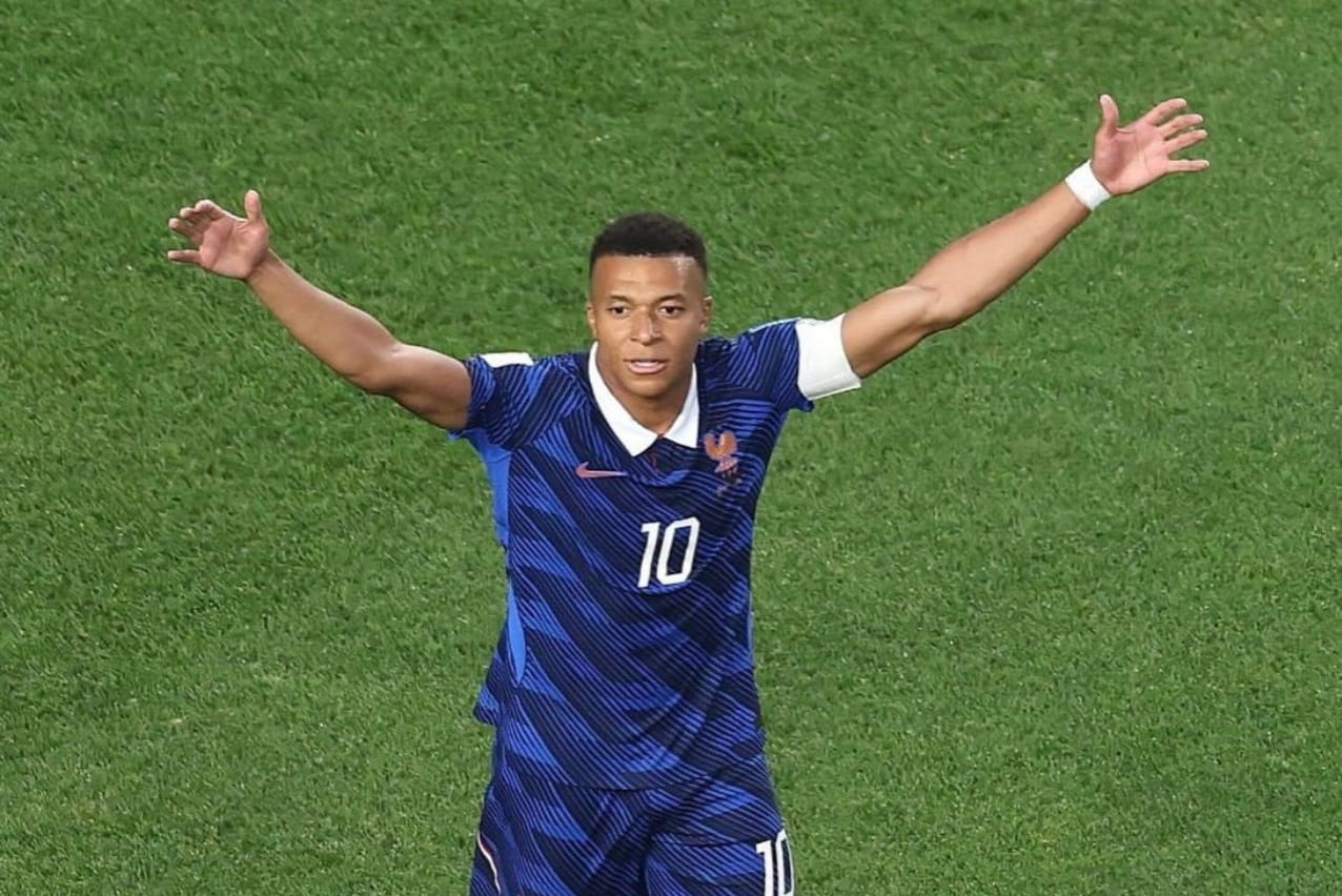 French soccer player with jersey number 10 raises arms in triumph on green field