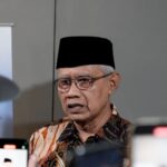Senior indonesian man in batik shirt and black peci hat speaks to reporters smartphones raised around him