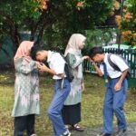 Four students in uniforms outdoors two girls in hijabs and two boys bowing to each other as a respectful greeting
