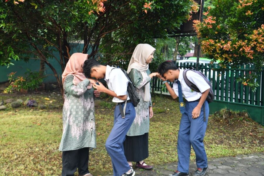 Four students in uniforms outdoors two girls in hijabs and two boys bowing to each other as a respectful greeting