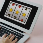 Laptop screen shows a three reel slot machine with yellow stars and red sevens on a pink background
