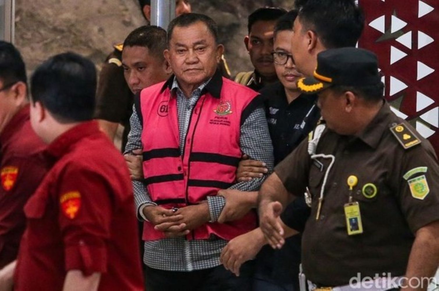 15gkorupsi1 catrawarta Older man in a pink vest being escorted by uniformed officers through a crowd