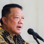 Man in a patterned batik shirt speaking into a microphone at a podium during a public event