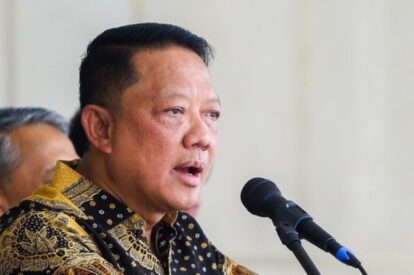 Man in a patterned batik shirt speaking into a microphone at a podium during a public event
