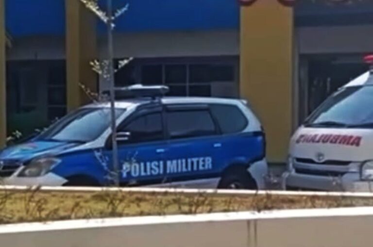 Military police car (Polisi Militer) in blue and white, parked near a building with yellow columns; emergency vehicle nearby