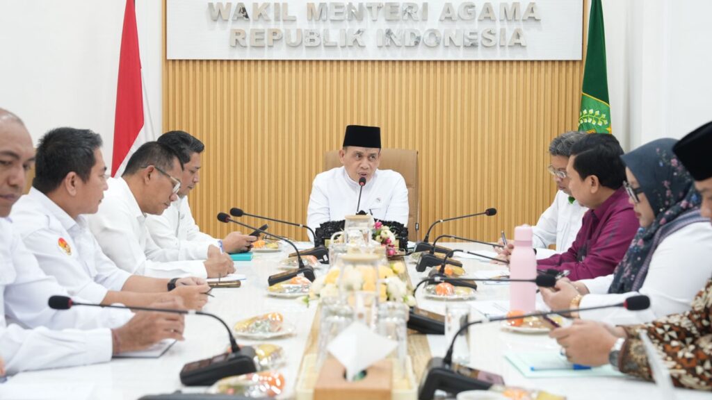 Formal meeting of indonesian officials around a long conference table central speaker at the head microphones and snacks visible backdrop reads wakil menteri agama republik indonesia