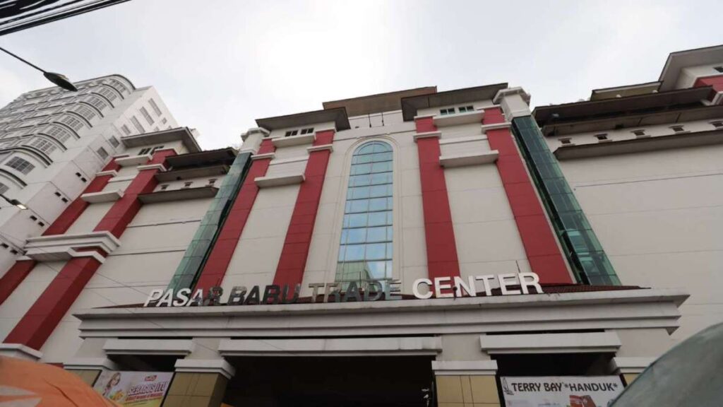 Facade of pasar baru trade center with red vertical accents and a tall arched window in the center