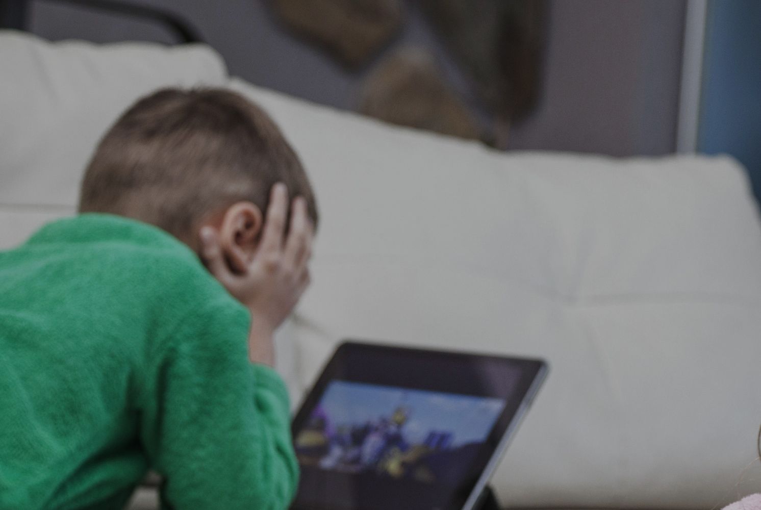 17ganak catrawarta Child in a green shirt lies on a sofa head in hands looking at a tablet screen