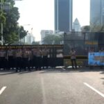Line of uniformed police officers standing behind a barricade across a city street blocking traffic with polisi signage visible