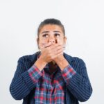 Woman covering her mouth with both hands looking upward in a surprised or worried expression