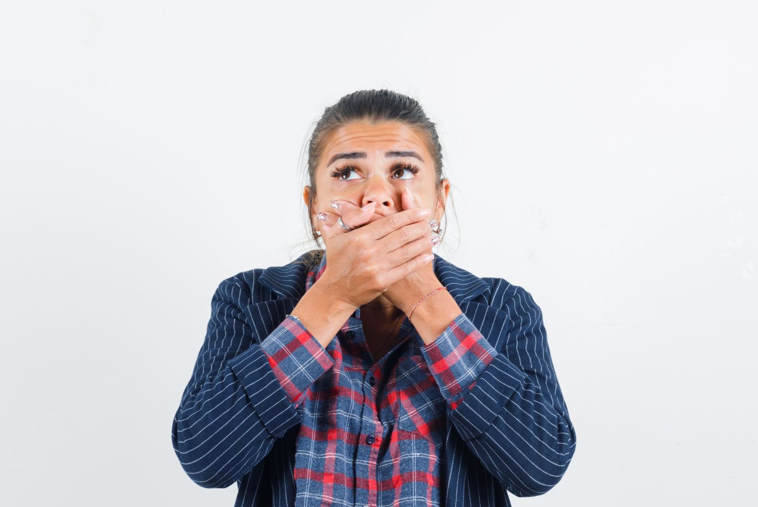 Woman covering her mouth with both hands looking upward in a surprised or worried expression