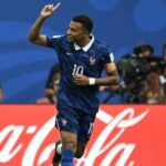 France national team footballer wearing number 10 raises his arm in celebration on the pitch cocacola ad boards in the background
