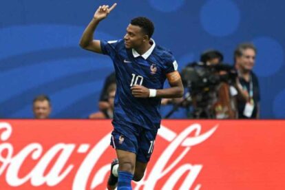 France national team footballer wearing number 10 raises his arm in celebration on the pitch, Coca‑Cola ad boards in the background.