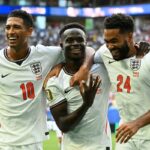 Three england players celebrate together on the pitch smiling with arms around each other after a goal stadium cheering in the background