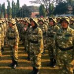 Group of soldiers in camouflage uniforms standing in formation on a grassy field on a sunny day