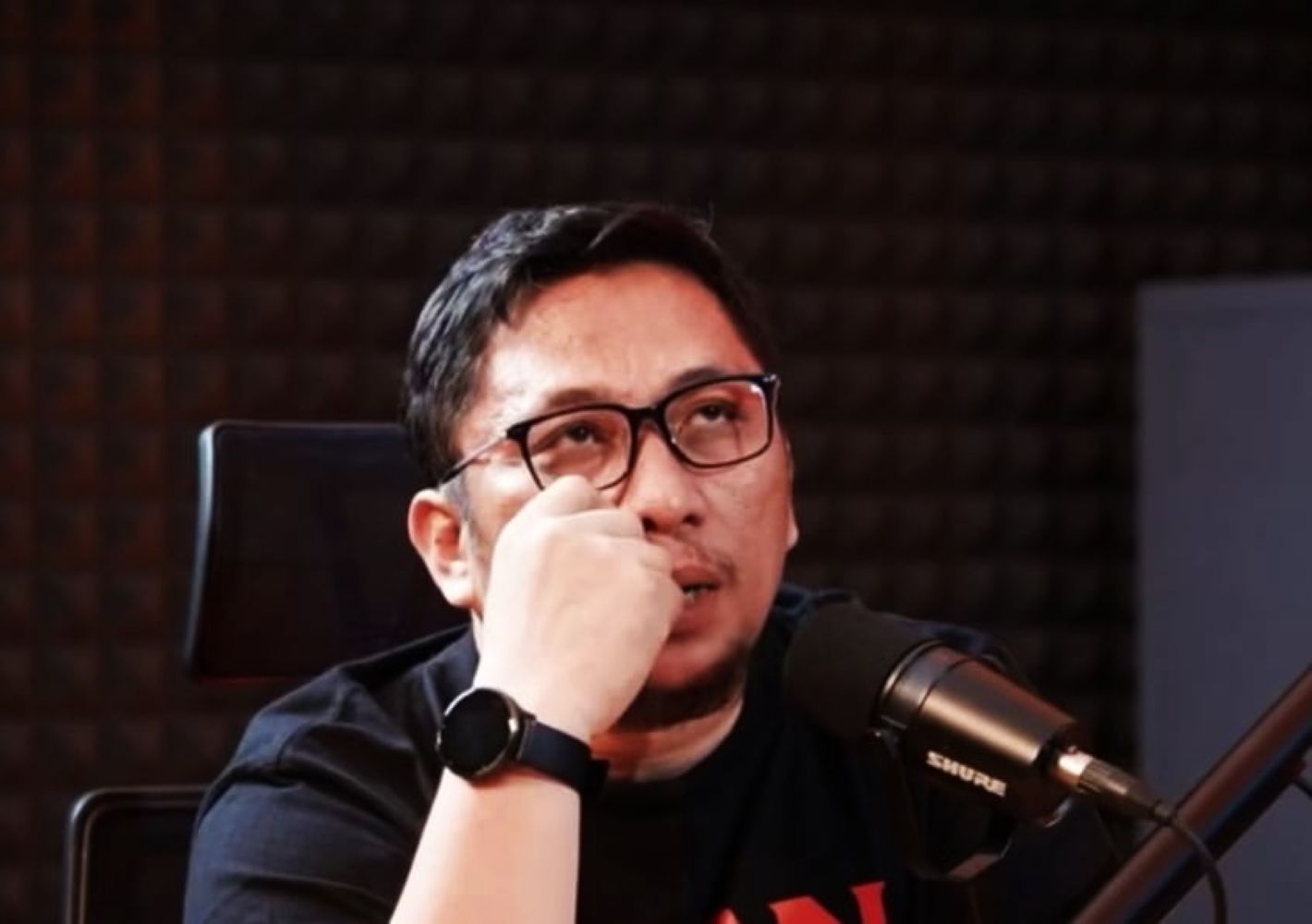 20gferi catrawarta Man wearing glasses and a black shirt sits at a microphone in a recording studio