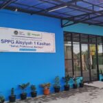 Blue building exterior with a glass entry and a large sign reading spg aisyiyah 1 kasihan near a row of potted plants along the wall