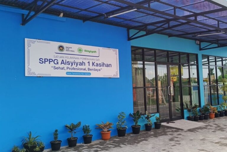 Blue building exterior with a glass entry and a large sign reading 'SPG Aisyiyah 1 Kasihan' near a row of potted plants along the wall.