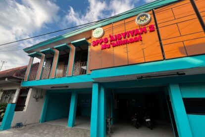 Colorful two-story building with turquoise columns and an orange wall panel, featuring bold signage at the top (educational facility).