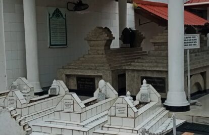 Row of white marble grave plots with stepped, pyramid-like markers in a sheltered courtyard.