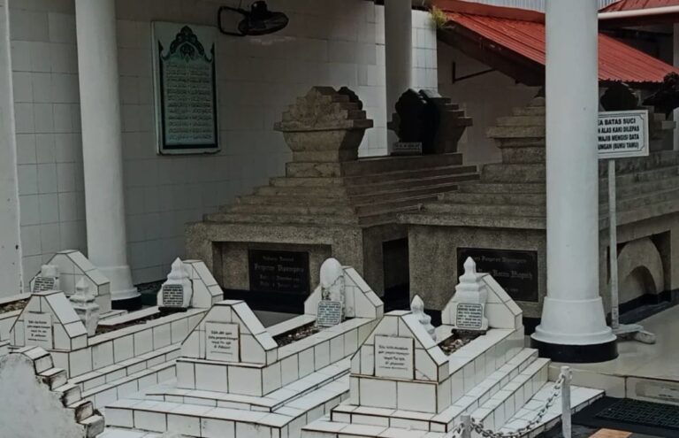 Row of white marble grave plots with stepped, pyramid-like markers in a sheltered courtyard.