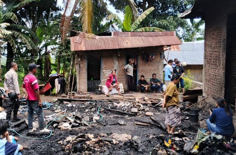 21grumah catrawarta Villagers gather around charred rubble outside a small brick house with a red corrugated roof in a tropical setting