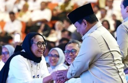 Smiling woman in a hijab shakes hands with a man wearing a traditional cap at a crowded event.
