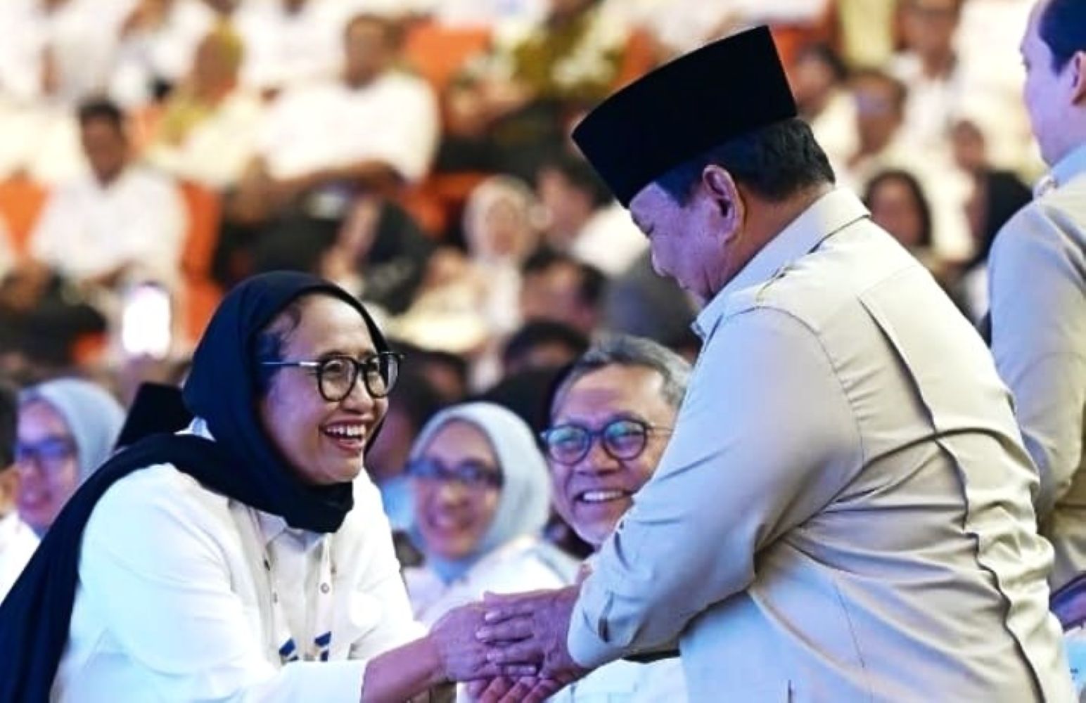 22gpamit catrawarta Smiling woman in a hijab shakes hands with a man wearing a traditional cap at a crowded event