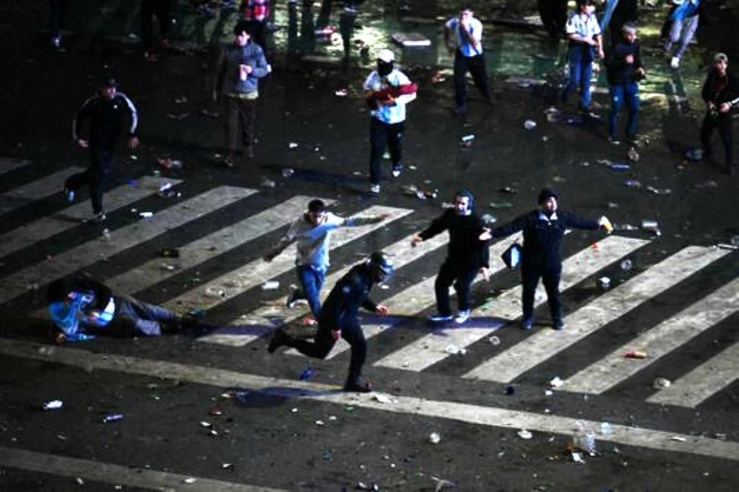 People running across a crosswalk at night with litter and debris scattered on the street