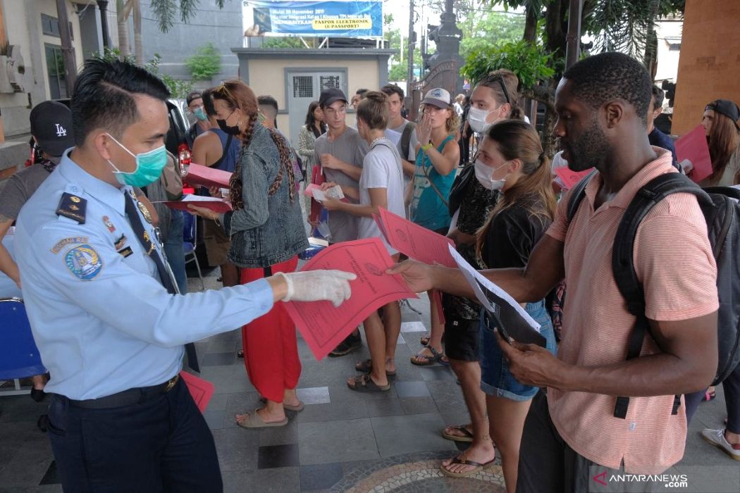 23gtarif1 catrawarta Uniformed officer wearing a mask hands pink documents to people lined up outdoors