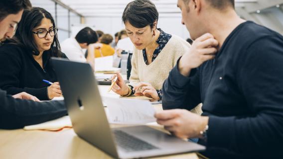 Group of diverse colleagues collaborating around a laptop reviewing papers at a bright table in a coworking space