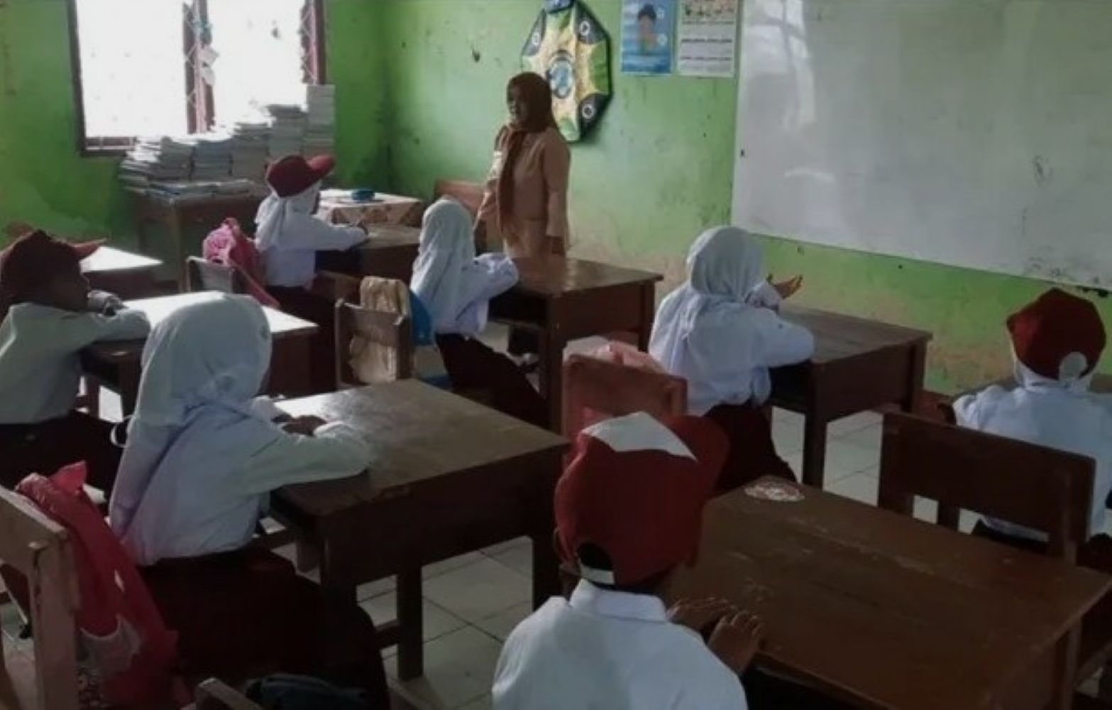 Teacher standing at the front of a small classroom as students sit at wooden desks and listen