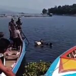 People on a colorful boat watching a person swimming or rescuing in calm water near the shore