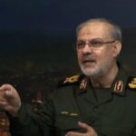 Military officer in a dark green uniform with gold insignia speaks on a set gesturing with his right hand