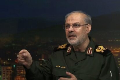 Military officer in a dark green uniform with gold insignia speaks on a set gesturing with his right hand