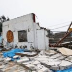 Ruined concrete building with collapsed walls scattered bricks blue tarps and leaning metal beams amid debris