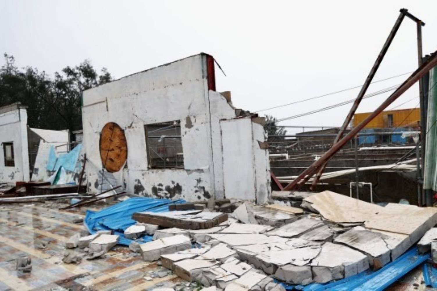Ruined concrete building with collapsed walls scattered bricks blue tarps and leaning metal beams amid debris
