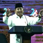 Indonesian official speaking at a lectern with hands raised in a formal setting