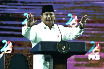 Indonesian official speaking at a lectern with hands raised in a formal setting