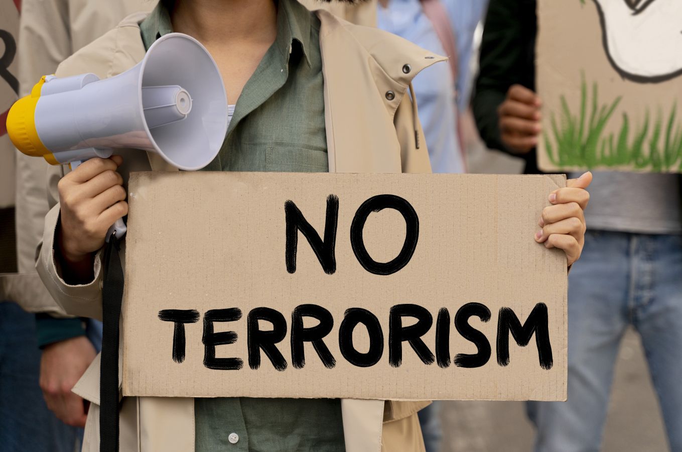 Protester holding a cardboard sign that reads no terrorism with a yellow and gray megaphone in hand