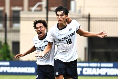 Georgetown soccer players celebrate on the field one in the foreground with arm extended outward and teammates behind him