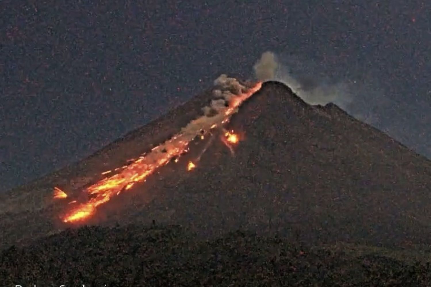 3gmerapi catrawarta Volcano erupting at night with lava flowing down its slope and a small plume of smoke