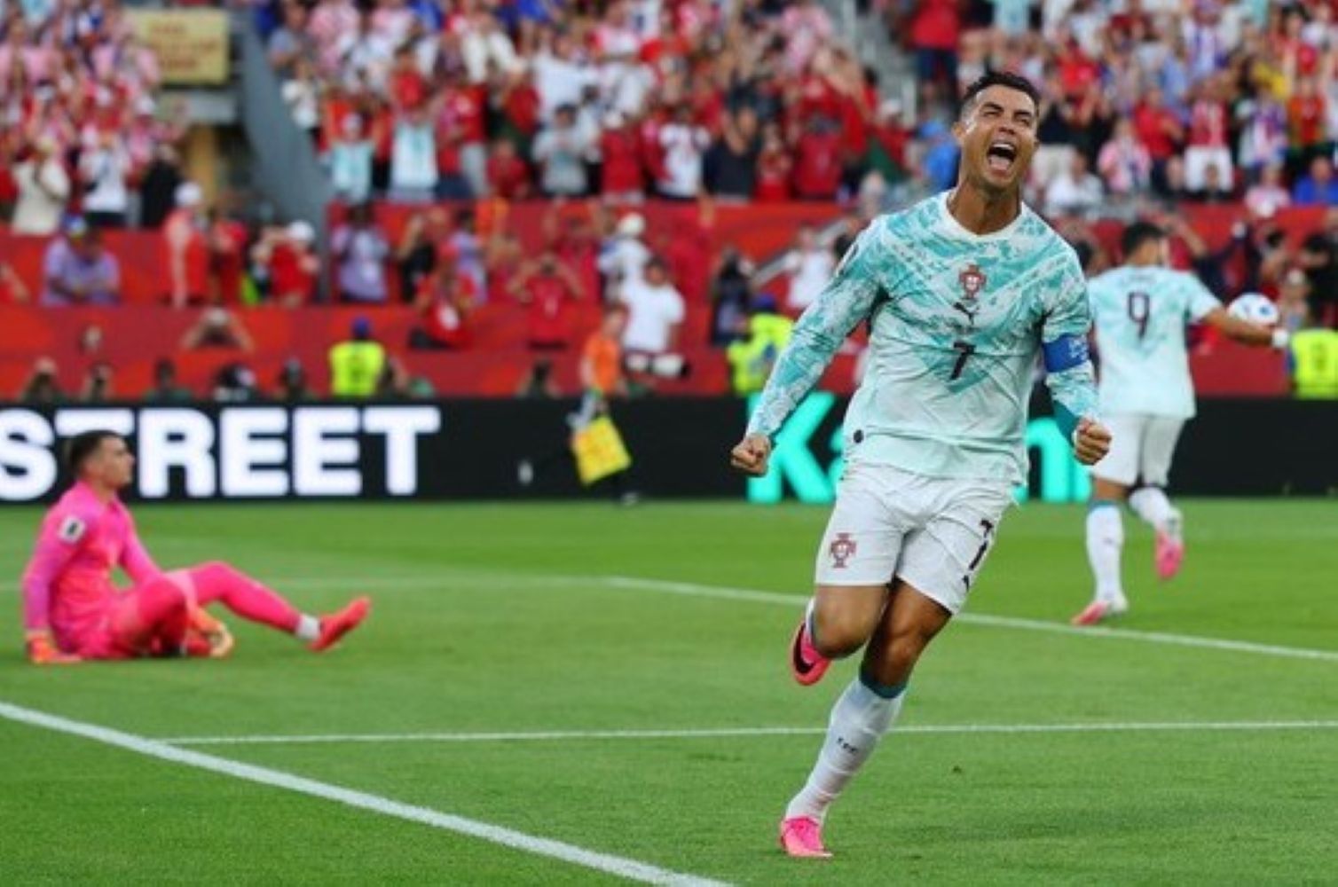 3gronaldo1 catrawarta Soccer player in portugals white and green kit celebrates a goal on the field with a pink clad goalkeeper on the ground behind him and a cheering crowd in the stands behind